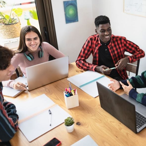 teenage students sitting at table studying and talking